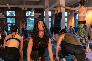 Diverse group of people in yoga class. An elated woman is seen in lying cobra pose during class dedicated to 108 rounds of surya namaskar, exercises to promote health and well being.