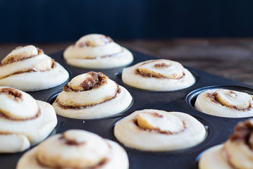 Homemade tall cinnamon roll rising in a muffin tin. Selective focus on center with blurred foreground and background.