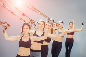 Obraz premium Group of five strong woman in black sportswear workout with TRX strap