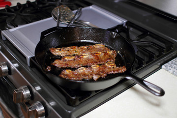 Korean style BBQ short ribs, known as Kalbi, on a cast iron skillet in a home kitchen.