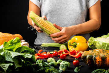 Woman peeling a corn cob, cooking different vegetables. Healthy vegetarian food concept.