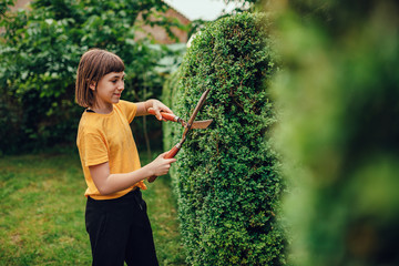 Girl pruning hedge with hand shears