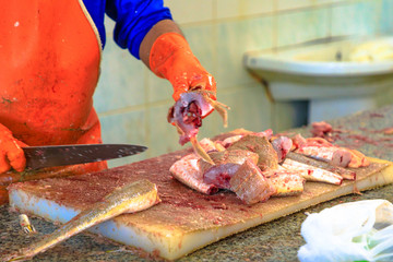 Details of worker cleans and cuts fresh fish at Al Khor Fish Market located near to corniche in Qatar, Middle East, Arabian Peninsula. Closeup of tuna fish on wooden cutting board.