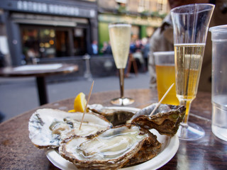 Wide closeup of a plate of raw oysters served with sparkling Prosecco wine outdoors at Borough Market. London, United Kingdom. Travel and seafood cuisine.