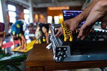 Diverse group of people in yoga class. The hands of a gym instructor are viewed up close, at the front of a workshop dedicated to yogic moves, operating music as people are seen in downward dog pose.