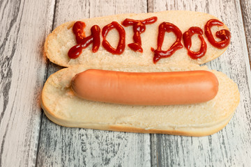 Hot dog with a boiled sausage on light wooden background. The inscription ketchup Hot-dog. Top view. Macro