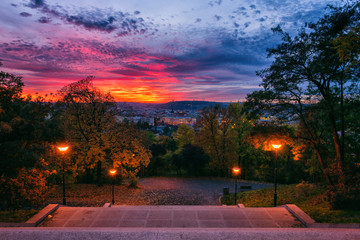 Fiery sunset view of Prague from Vitkov hill with autumn park, scenic cytiscape with city lights, Zizkov district, Czech Republic, travel background