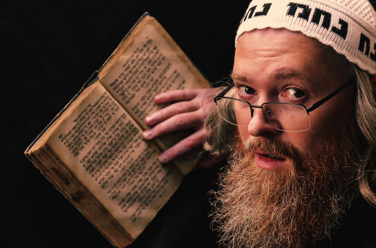 A Hasidic Jew reads Siddur. Religious orthodox Jew with a red beard and with pace in a white bale praying. On the bale is an inscription Rabbi Nahman from Uman. Closeup