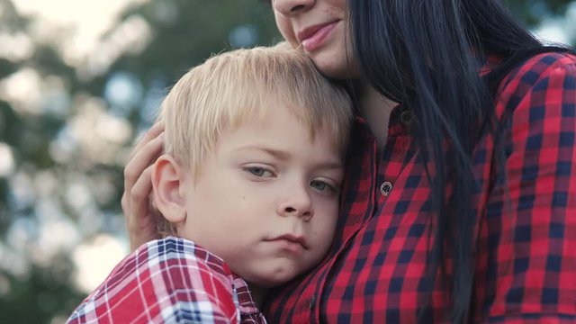 happy family mom and son sad child concept. mom tender childhood video. slow motion lifestyle video. a mom brunette girl protects caress gently hugs takes care of the son boy blonde outdoors