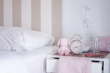 Girl's bedroom. A girl's bed room with pink decoration on the desk with selective focus on the pink alarm clock next to the pink rabbit plush doll.