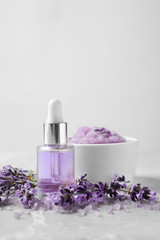 Natural cosmetic oil, bath salt, scrub and lavender flowers on grey marble table, space for text