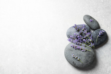 Spa stones and lavender flowers on grey table, flat lay. Space for text