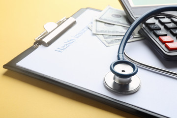 Clipboard with with medical insurance form, money, calculator and stethoscope on yellow background, closeup