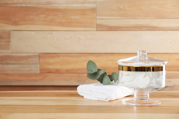 Fototapeta na wymiar Decorative glass jar with cotton pads and towel on table against wooden background. Space for text