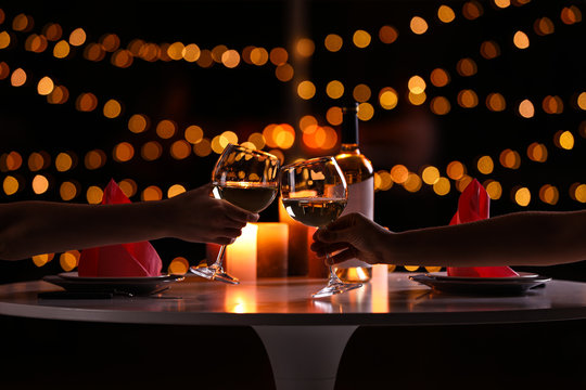 Young couple with glasses of wine having romantic candlelight dinner at table, closeup