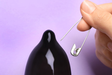 Woman piercing inflated condom with pin on violet background, closeup. Safe sex