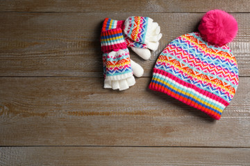 Obraz na płótnie Canvas Warm knitted hat and mittens on wooden background, flat lay. Space for text