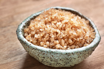 Bowl with brown sea salt on wooden table, closeup. Spa treatment