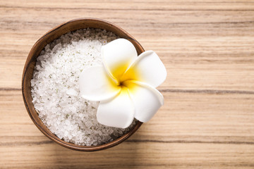 Fototapeta na wymiar White sea salt for spa scrubbing procedure and flower on wooden background, top view