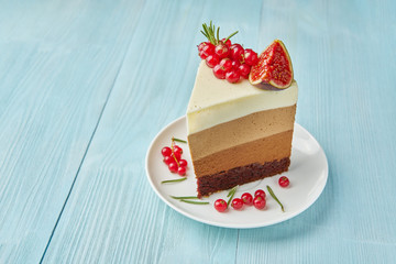 A piece of homemade cake decorated with red currants, figs, cinnamon and rosemary on a light blue wooden table.