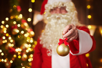 Closeup of Santa Claus hands with christmas ball decoration, sitting indoor near decorated xmas tree with lights - Merry Christmas and Happy Holidays!