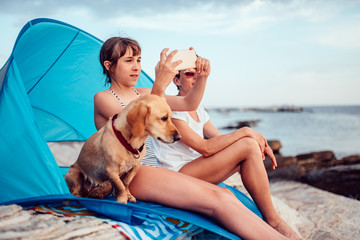 Girl taking photo with smartphone while sitting inside beach tent with mother and dog