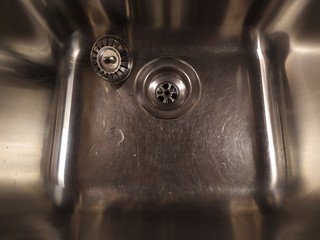 Shiny metal sink with a plug. Silver color. Scratch the surface. The view from the top at a slight angle.