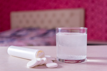 The effervescent tablet dissolves in a glass of water. A handful of pills on the table. Blurred background the bed in the bedroom. Treatment of viral diseases. Help with depression and insomnia