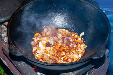The process of cooking Asian pilaf on fire. Meat is fried in a cauldron, close-up.