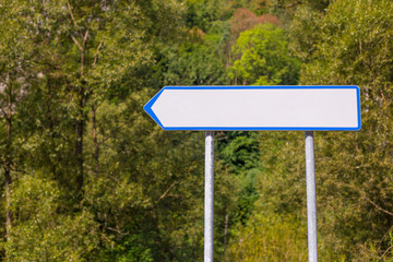 Blank white directional arrow sign on nature background. Blank road sign on the road