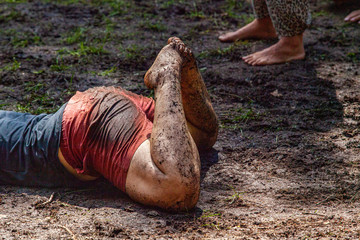 Diverse people enjoy spiritual gathering A young woman is seen closeup, laying on her stomach in mud and earth during a celebration of intercultural practices and rituals, with room for copy