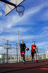 Two young bearded basketball player athletes run along an open sports field to the basketball hoop. Dribbling and attacking the opponent's basketball hoop. Travelling before the jump with a ball.