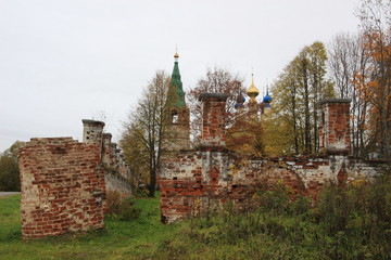 Fototapeta premium Path in old fence to cemetery, stone belfry and orthodox church with domes in cloudy autumn day