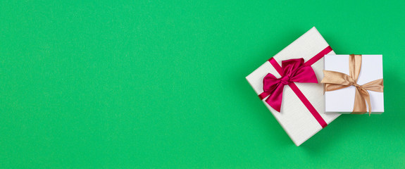 Two gift present boxes with ribbon on green background, top view