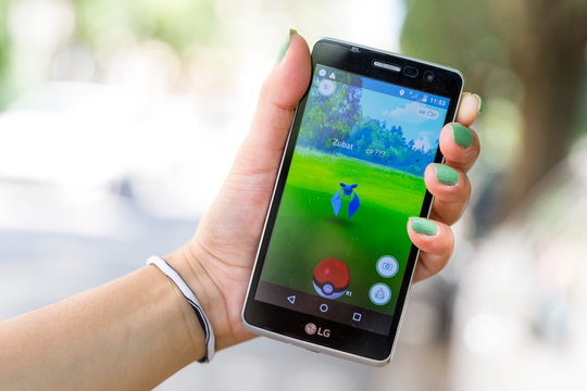 Sofia, Bulgaria - July 23, 2016: Woman holds in her hand a mobile phone showing on screen Pokemon Go augmented reality mobile game. Playing in the park. Zubat.