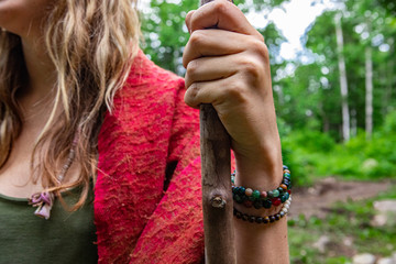 Diverse people enjoy spiritual gathering A close up view on the arm and wrist of a young shamanic girl with long blonde hair, wearing sacred prayer beads and holding a long wooden stick in nature.