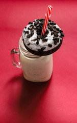 donut with cookie pieces on the cup of milk with the straw, red background. 