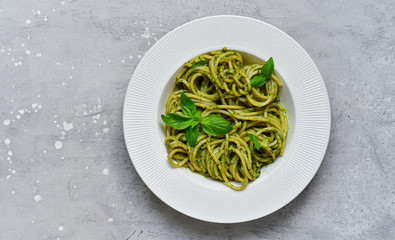 Pasta spaghetti pesto with fresh basil and olive oil on a white craft plate, gray stone background. Italian cuisine recipe, traditional  Italian dish