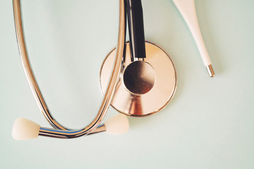The black stethoscope and thermometer on a turquoise background
