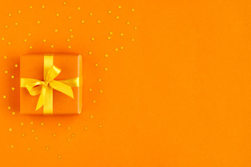 Gift box with ribbon and bow on orange background with gold stars . Top view and space for text.