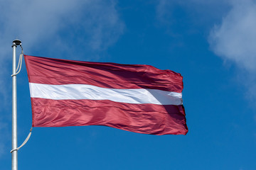 Naklejka na ściany i meble Flag of the Republic of Latvia. Flag of Latvia against the blue sky. Copy space.