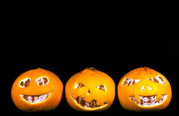 Grapefruit, tangerines and oranges are isolated on a black background in the form of a halloween pumpkin. A scary face is carved on grapefruit, tangerines and oranges.