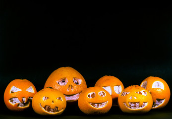 Grapefruit, tangerines and oranges are isolated on a black background in the form of a halloween pumpkin. A scary face is carved on grapefruit, tangerines and oranges.