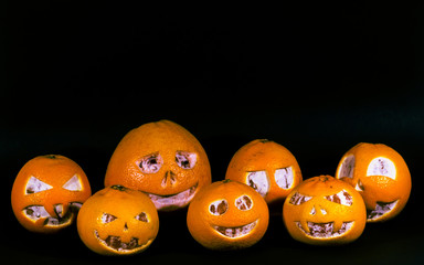 Grapefruit, tangerines and oranges are isolated on a black background in the form of a halloween pumpkin. A scary face is carved on grapefruit, tangerines and oranges.