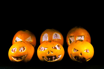 Grapefruit, tangerines and oranges are isolated on a black background in the form of a halloween pumpkin. A scary face is carved on grapefruit, tangerines and oranges.