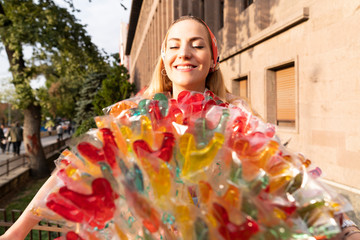 Girl holding a lollipop. Beautiful happy blond girl in the street. Young woman eating a piece of candy. 