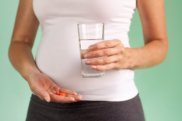 A pregnant girl holds a glass of water and pills in her hands. Maintaining the health of mother and baby.