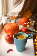 Cup of tea with lemon against pumpkins, apples and autumn decorations on the window.