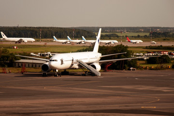 A white plane is parked at the airport with an attached ramp. Organization of storage and maintenance of aircraft at the airport. Airport Logistics.