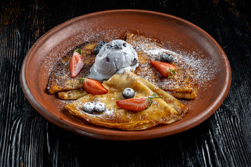 Pancakes with ice cream, with blueberries and strawberries, sprinkled with icing sugar.